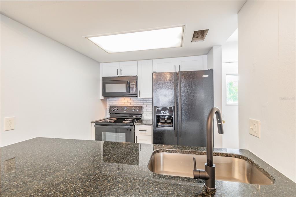 A kitchen features dark granite countertops, a stainless steel sink, and black appliances — 4907 W MCELROY AVENUE UNIT H209, TAMPA, FL