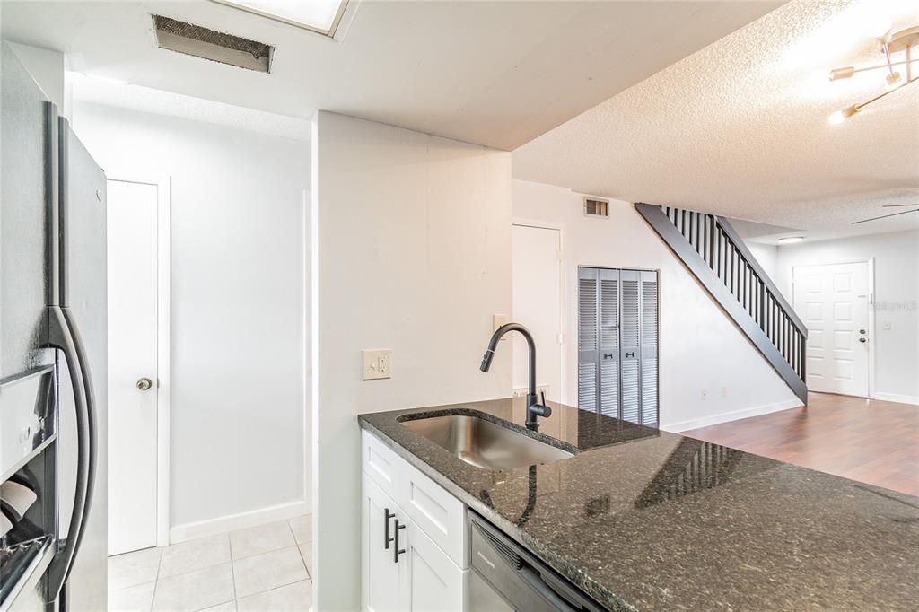 A kitchen with dark granite countertops and white cabinets overlooks a living area with stairs — 4907 W MCELROY AVENUE UNIT H209, TAMPA, FL