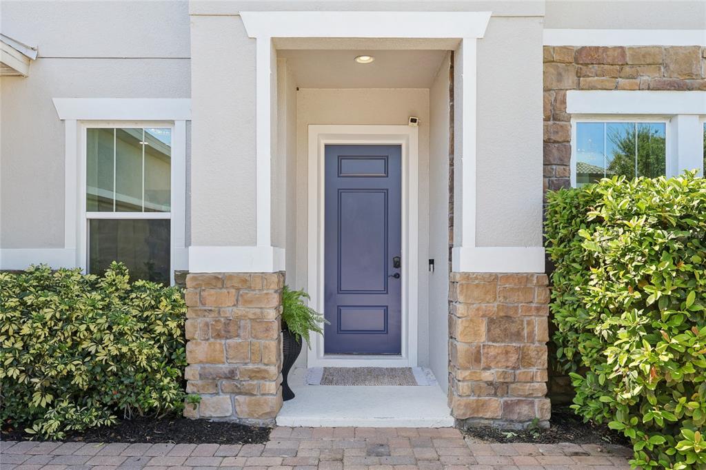A blue front door is centered between stone-accented walls and two large green bushes — 14612 GLADE HILL PARK WAY, WINTER GARDEN, FL