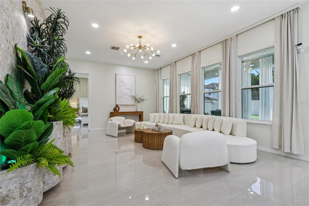 A bright living room features white curved sofas, a wooden coffee table, and large potted plants — 14612 GLADE HILL PARK WAY, WINTER GARDEN, FL