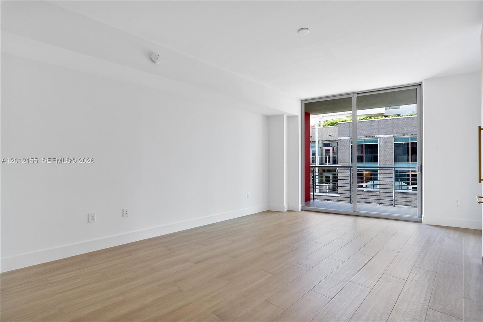 An empty room with light wood-look flooring, white walls, and a sliding glass door to a balcony — 90 NE 32 St # 413, Miami FL 33127, MIAMI, FL