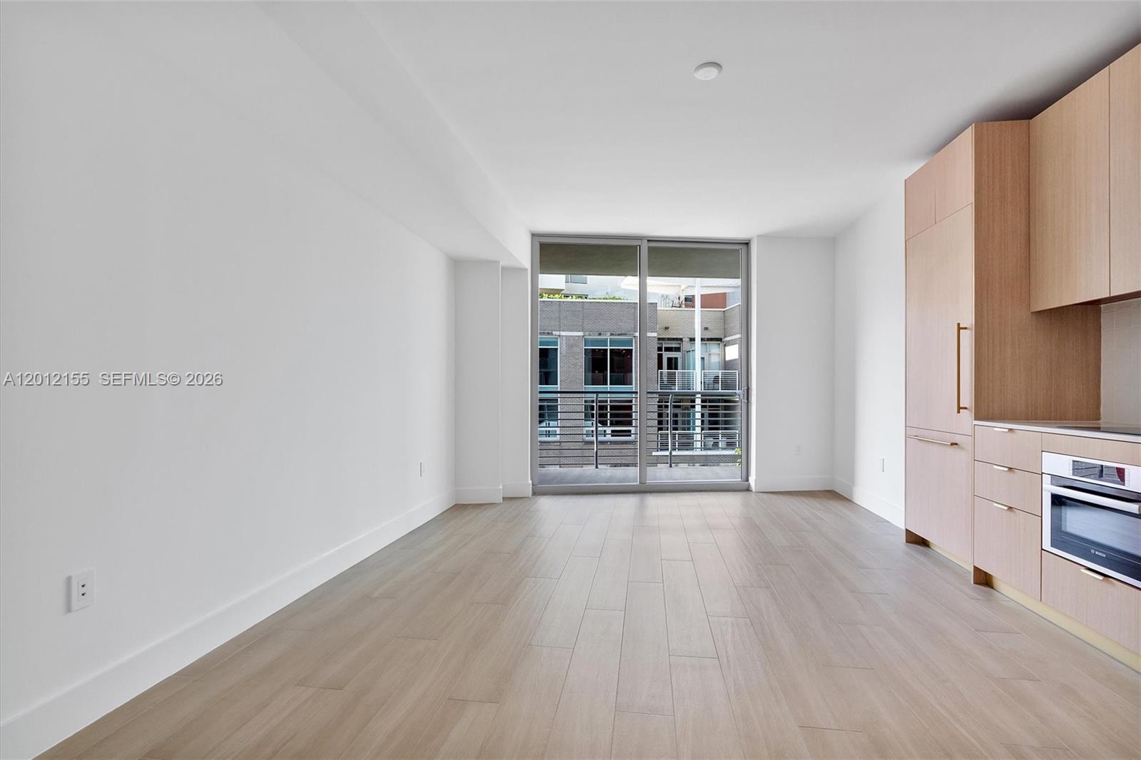 A modern, unfurnished room features light wood flooring, white walls, and a built-in kitchen area — 90 NE 32 St # 413, Miami FL 33127, MIAMI, FL