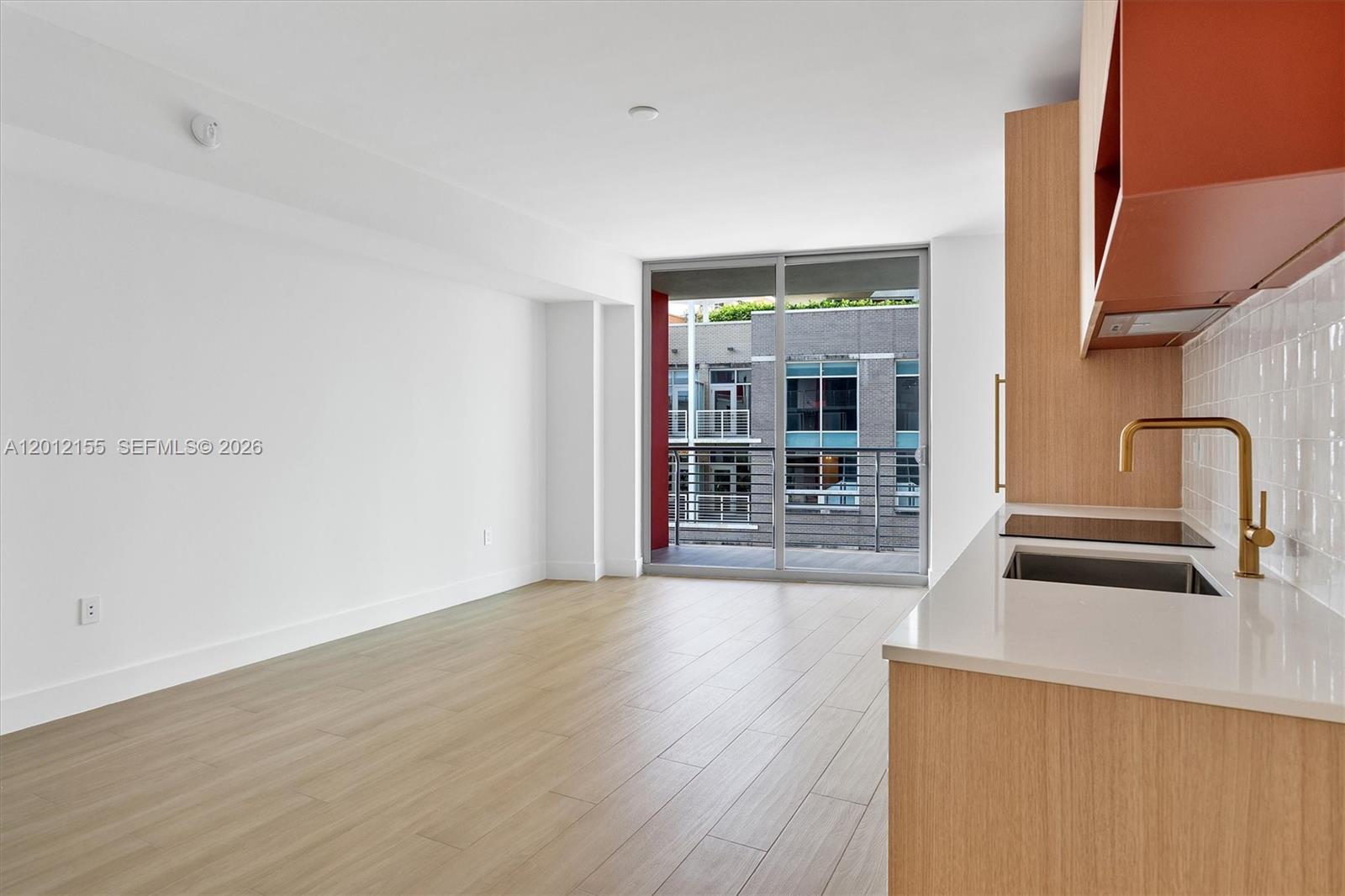 A modern kitchen with light wood cabinets and a gold faucet overlooks an empty living area — 90 NE 32 St # 413, Miami FL 33127, MIAMI, FL