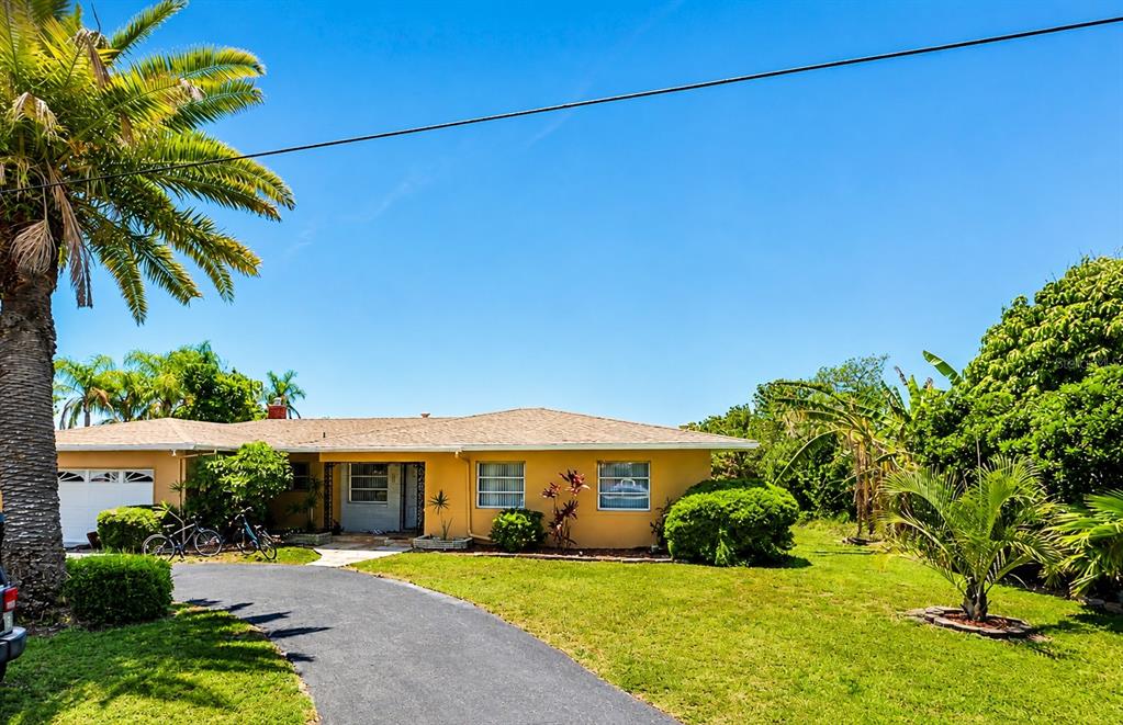The exterior of a yellow house features a wooden deck, stone patio, and palm trees — 5412 LEILANI DRIVE, ST PETE BEACH, FL