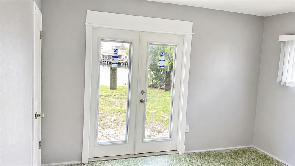 A room with gray walls, green carpet, and French doors looking out toward a canal — 5412 LEILANI DRIVE, ST PETE BEACH, FL
