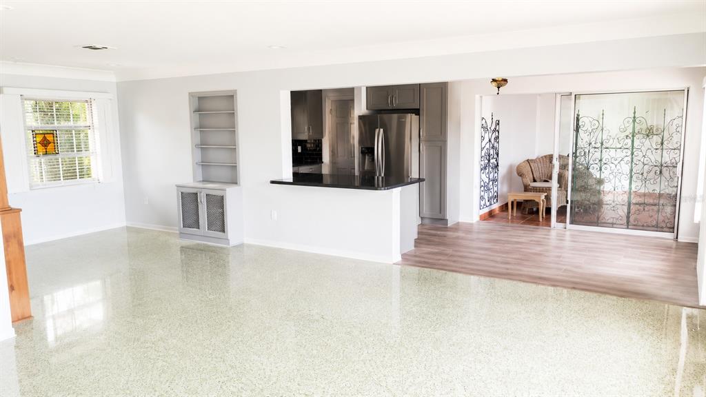 A living room with terrazzo flooring, built-in shelving, a kitchen pass-through, and a sunroom beyond — 5412 LEILANI DRIVE, ST PETE BEACH, FL
