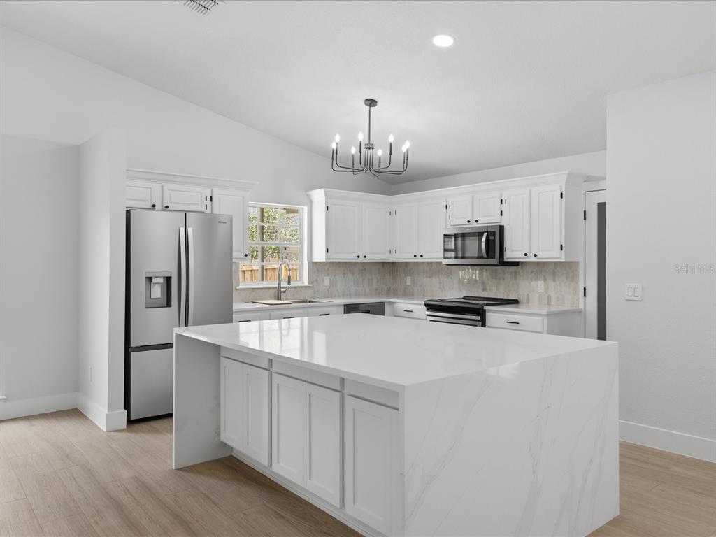 A modern kitchen features white cabinets, a large marble-topped island, and stainless steel appliances — 505 LAKE CHARM DRIVE, OVIEDO, FL