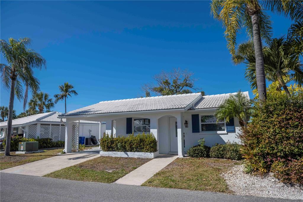 A white one-story house with a carport, tiled roof, and palm trees under a blue sky — 563 SPANISH DRIVE S, LONGBOAT KEY, FL