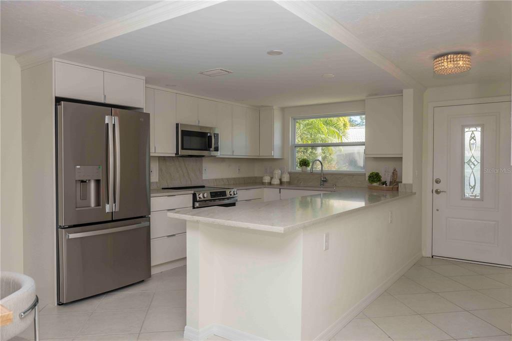 A modern kitchen features white cabinets, stainless steel appliances, and a peninsula with stone countertops — 563 SPANISH DRIVE S, LONGBOAT KEY, FL