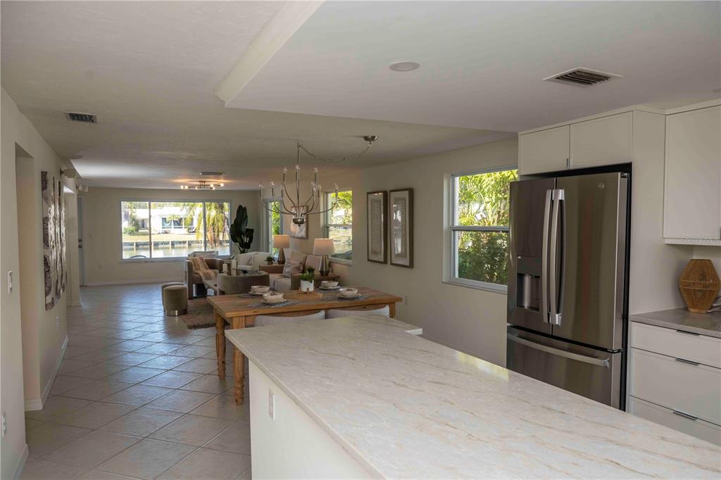 A kitchen island with a stone countertop overlooks a dining area and a living room — 563 SPANISH DRIVE S, LONGBOAT KEY, FL