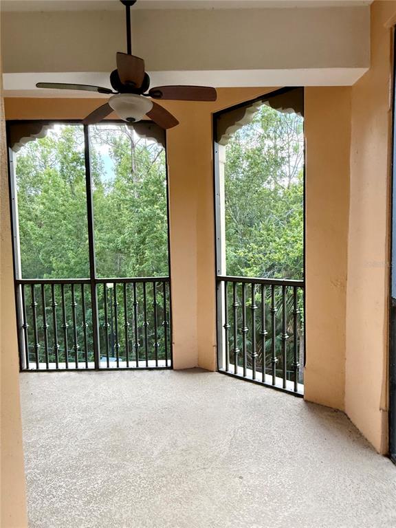 A screened-in balcony features a ceiling fan, concrete flooring, and views of surrounding trees — 501 MIRASOL CIRCLE UNIT 301, CELEBRATION, FL