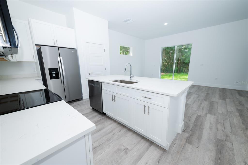 A modern kitchen features white cabinets, stainless steel appliances, a center island, and gray flooring — 9298 N MENDOZA WAY, CITRUS SPRINGS, FL