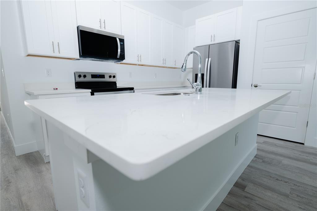 A modern kitchen features white cabinets, stainless steel appliances, and a large quartz-topped island — 9298 N MENDOZA WAY, CITRUS SPRINGS, FL