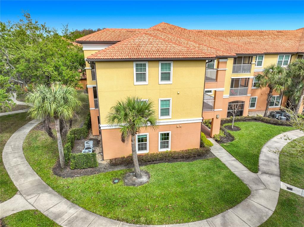 An exterior view of a three-story apartment building with yellow and orange stucco walls — 5471 VINELAND ROAD UNIT 7109, ORLANDO, FL