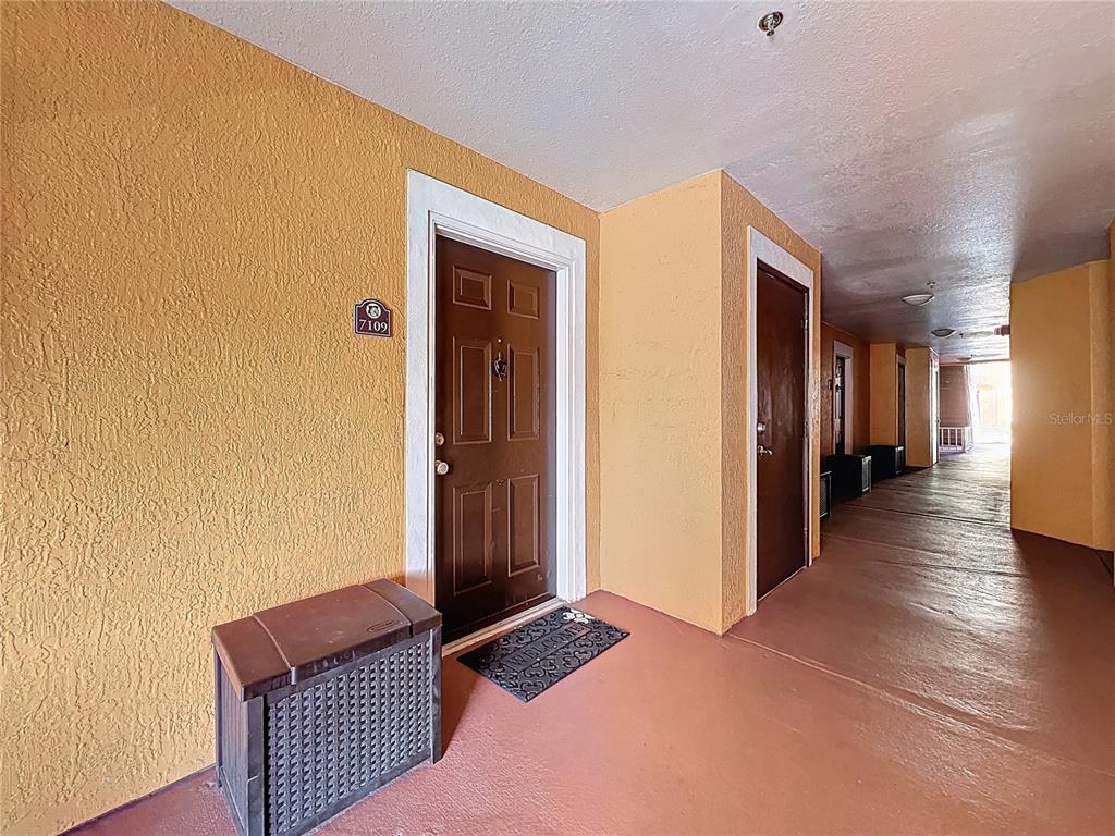 A brown front door with a unit number sign sits in an outdoor apartment hallway — 5471 VINELAND ROAD UNIT 7109, ORLANDO, FL
