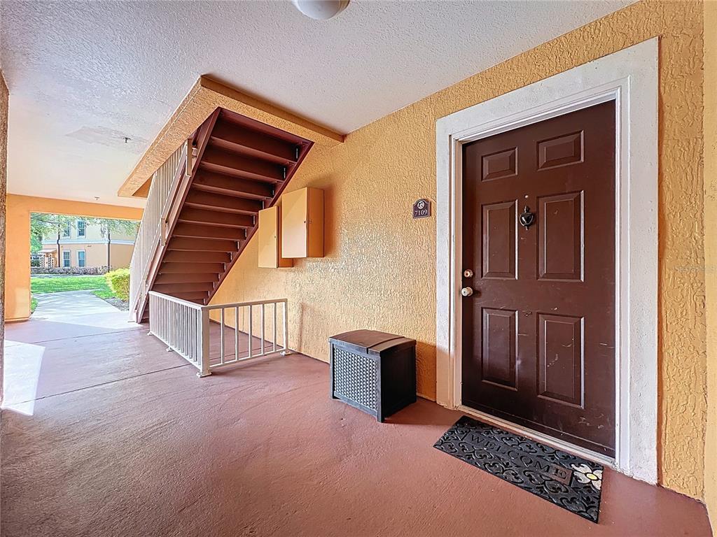 An exterior view of a residential building entrance featuring a brown door and staircase — 5471 VINELAND ROAD UNIT 7109, ORLANDO, FL