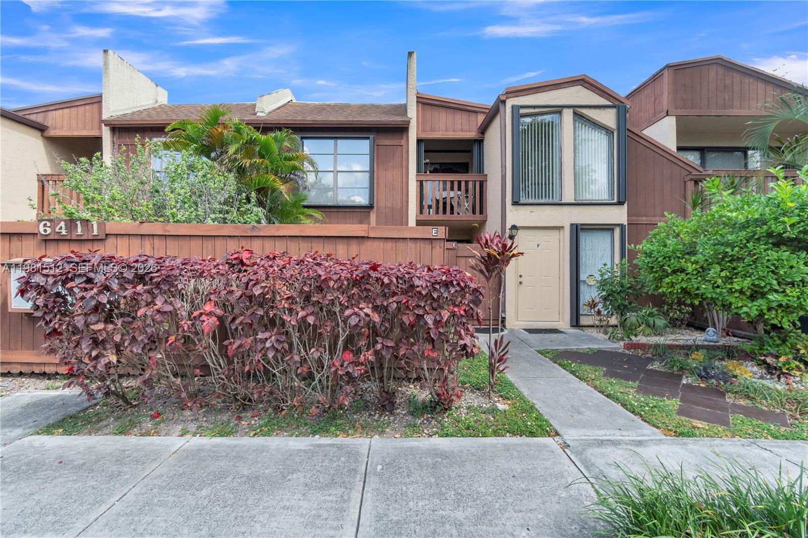 A two-story townhouse exterior features brown wood siding, a wooden fence, and a front walkway — 6411 SW 116th Ct, Miami FL 33173, MIAMI, FL