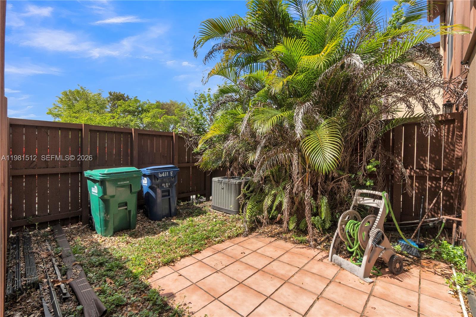 A fenced backyard features a tiled patio, a large palm tree, and two trash bins — 6411 SW 116th Ct, Miami FL 33173, MIAMI, FL