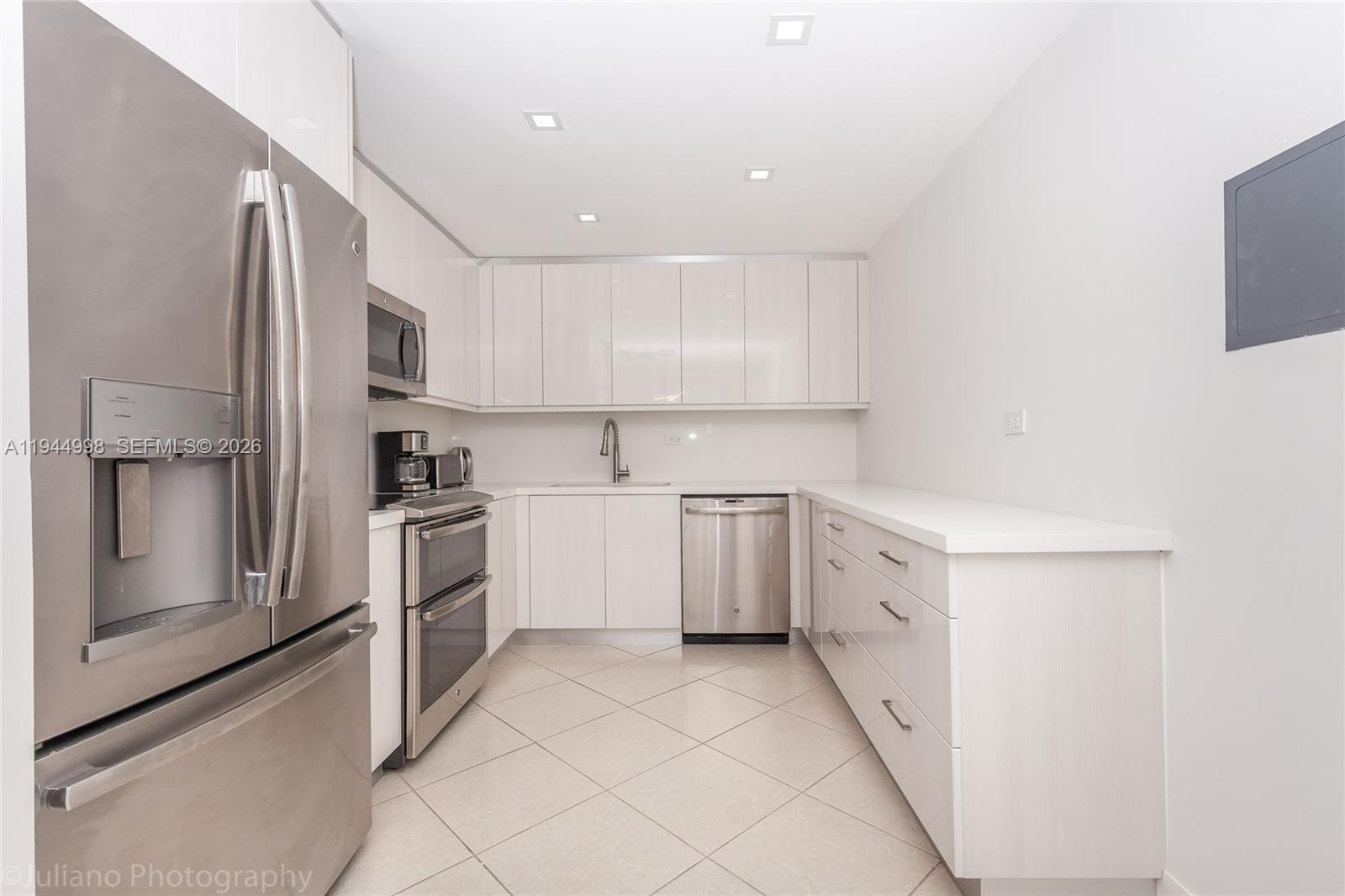 A modern kitchen features white cabinetry, stainless steel appliances, and light-colored tile flooring — 5555 Collins Ave # 9U, Miami Beach FL 33140, MIAMI BEACH, FL