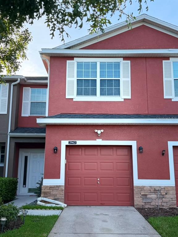 A two-story townhouse features a red stucco exterior, a single-car garage, and stone veneer accents — 2962 RODRICK CIRCLE, ORLANDO, FL