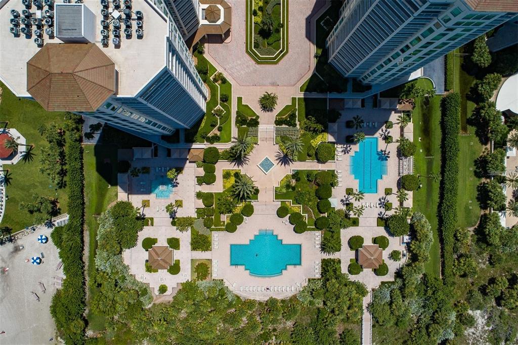 An aerial view shows two high-rise buildings with swimming pools, landscaped courtyards, and beach access — 1180 GULF BOULEVARD UNIT 906, CLEARWATER BEACH, FL