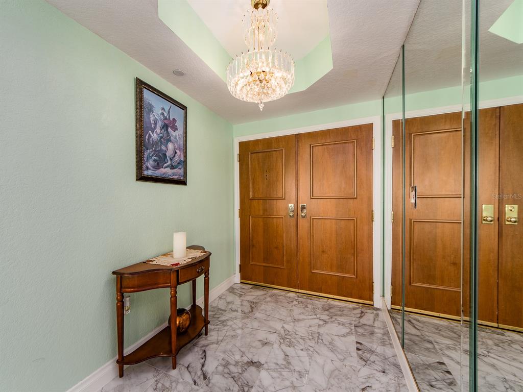 An entryway features a crystal chandelier, marble flooring, a wooden console table, and mirrored closet doors — 1180 GULF BOULEVARD UNIT 906, CLEARWATER BEACH, FL