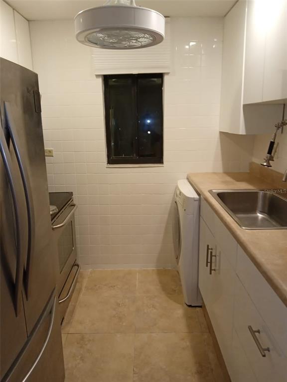 A galley kitchen features white cabinets, a stainless steel refrigerator, a sink, and a washer — 3242 SEMORAN BOULEVARD UNIT 25, ORLANDO, FL