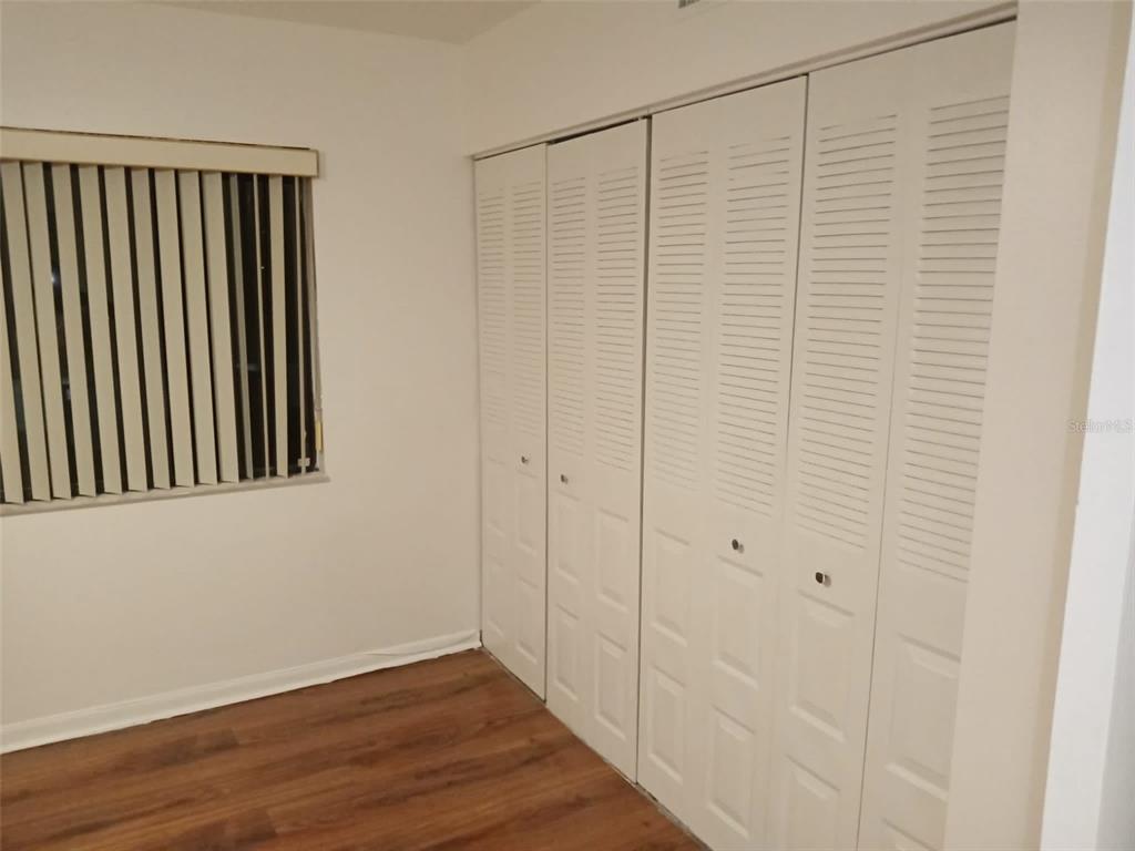 A bedroom features wood-look flooring, a window with blinds, and a four-panel louvered closet door — 3242 SEMORAN BOULEVARD UNIT 25, ORLANDO, FL