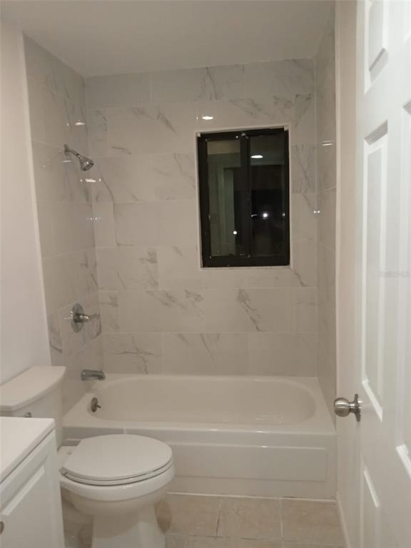 A bathroom features a white toilet, a bathtub with a shower, and marble-look wall tiles — 3242 SEMORAN BOULEVARD UNIT 25, ORLANDO, FL