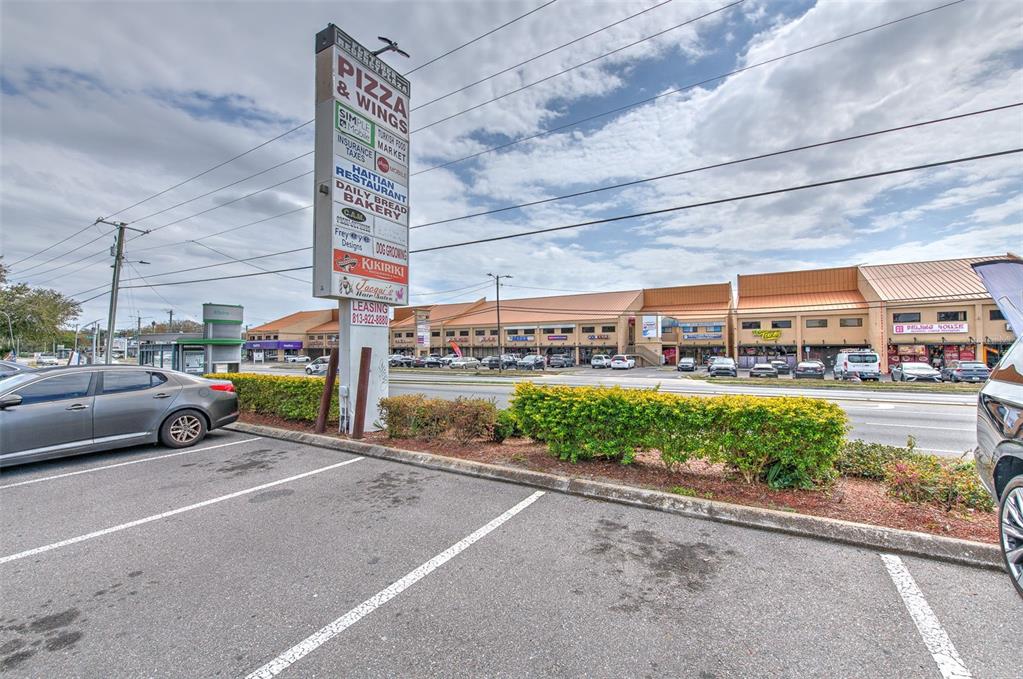 A parking lot sits in front of a commercial strip mall with a tall sign — 1402 E FLETCHER AVENUE UNIT 1406, TAMPA, FL