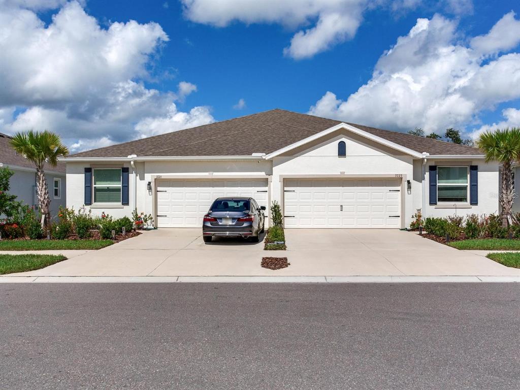 A duplex home with two garage doors, a parked car, and palm trees under blue skies — 3723 STORMY THISTLE PLACE, PLANT CITY, FL