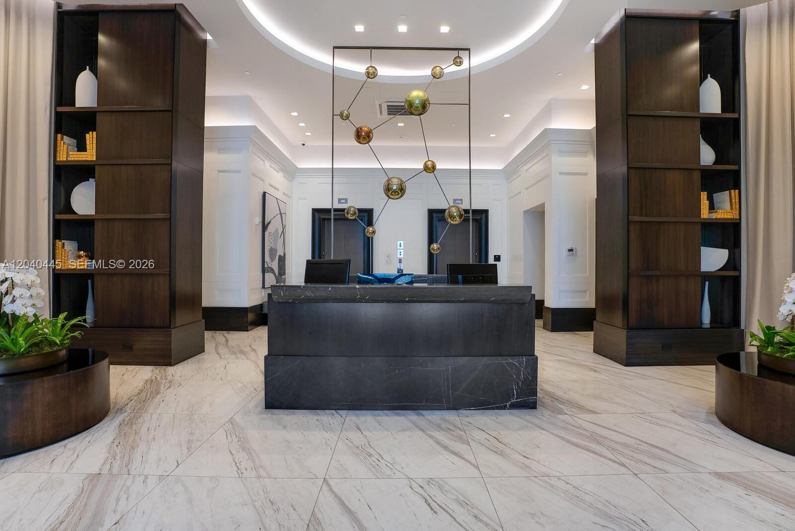 A modern lobby features a dark marble reception desk, symmetrical shelving, and a metallic sculpture — 275 Giralda Ave # 6C, Coral Gables FL 33134, CORAL GABLES, FL