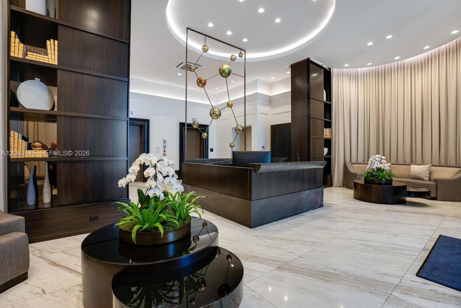 A modern lobby features a dark stone reception desk, marble floors, and decorative shelving units — 275 Giralda Ave # 6C, Coral Gables FL 33134, CORAL GABLES, FL