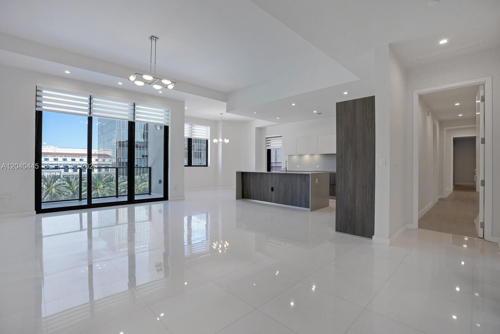 A modern, open-concept living area features white tile floors, a kitchen island, and balcony access — 275 Giralda Ave # 6C, Coral Gables FL 33134, CORAL GABLES, FL
