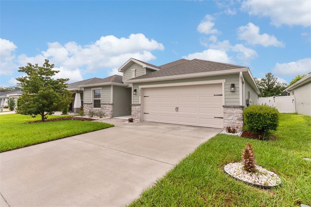 A single-story house with a beige garage, light green siding, and stone accents — 1944 HARVEST LANDING CIRCLE, LAKELAND, FL