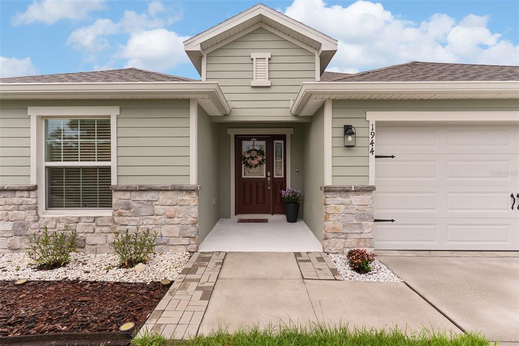 A single-story house exterior features light green siding, stone accents, and a white garage door — 1944 HARVEST LANDING CIRCLE, LAKELAND, FL