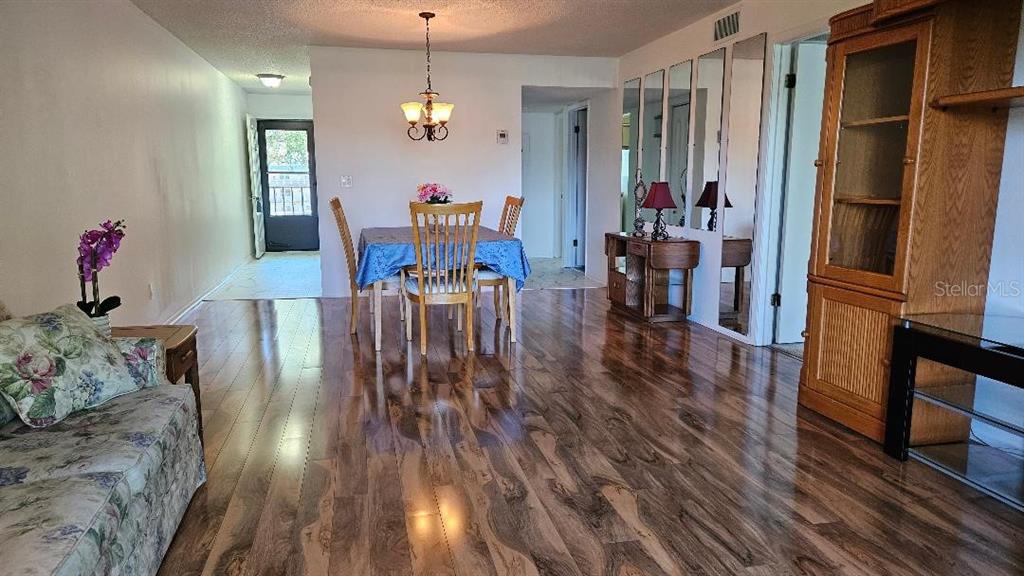 A dining area and living space feature wood-look flooring, a chandelier, and mirrored wall panels — 5920 80TH STREET N UNIT 308, ST PETERSBURG, FL