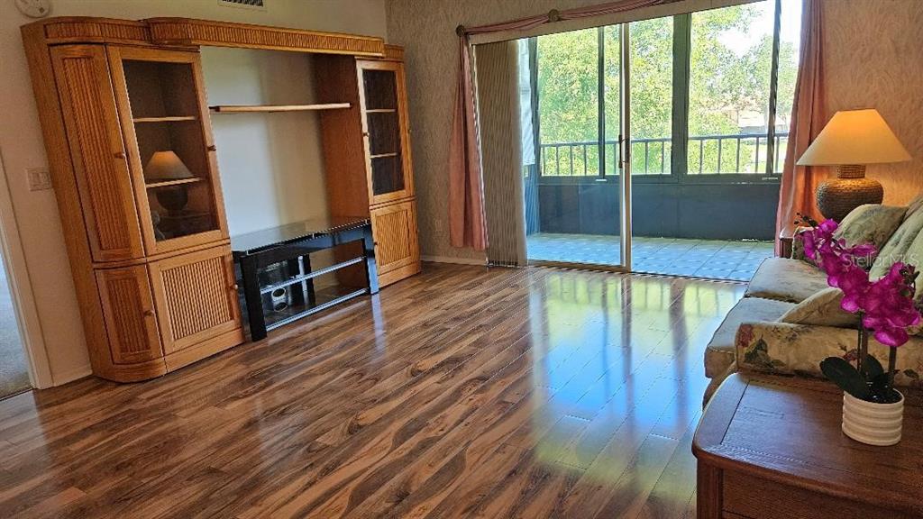 A living room features wood-look flooring, a large entertainment center, and a sliding glass door — 5920 80TH STREET N UNIT 308, ST PETERSBURG, FL