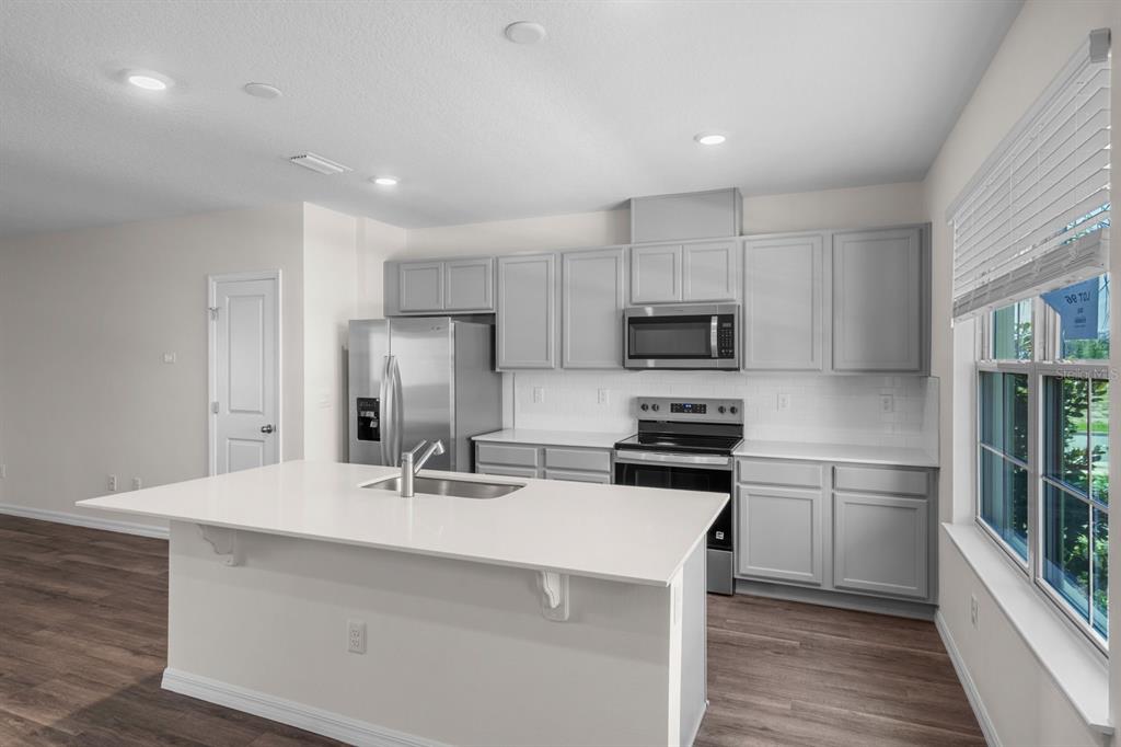 A modern kitchen features light gray cabinets, white countertops, stainless steel appliances, and an island — 16588 BARBOURS CREEK WAY, WINTER GARDEN, FL