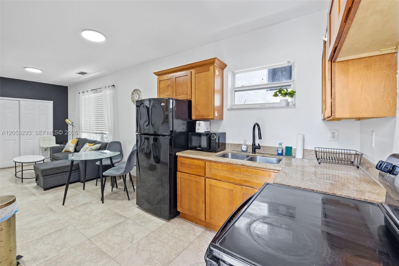 A kitchen with wooden cabinets, a black refrigerator, and a small dining area nearby — 417 NE 26th St # 5, Miami FL 33137, MIAMI, FL