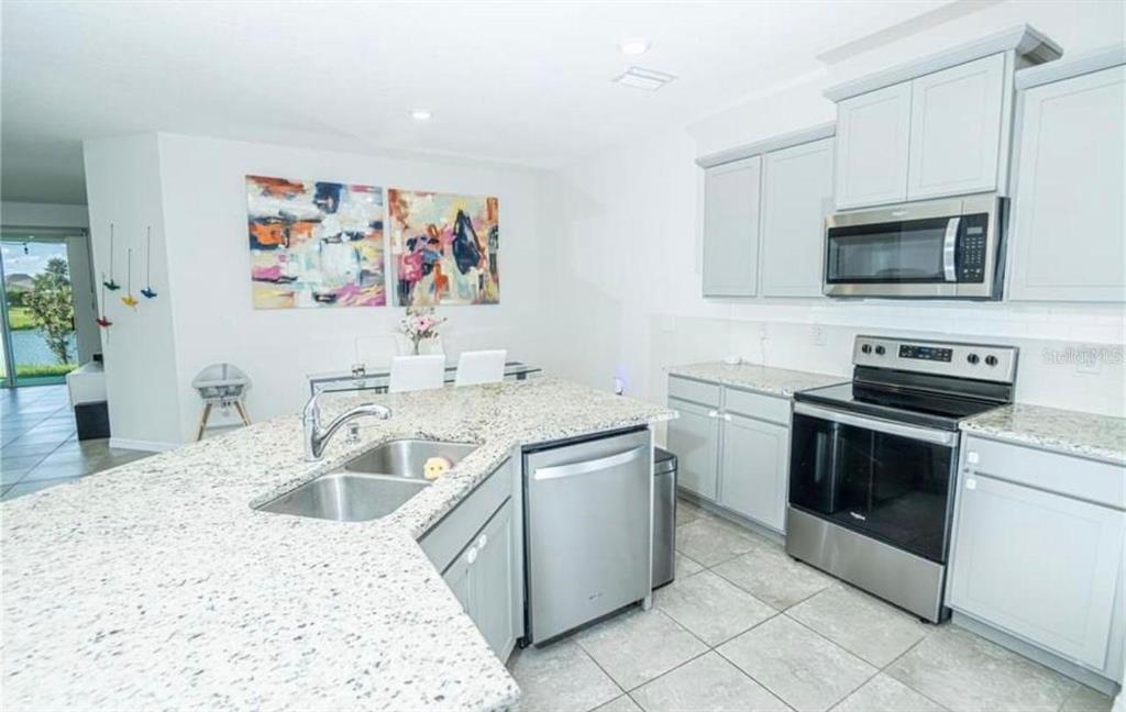 A kitchen with light gray cabinets, granite countertops, stainless steel appliances, and tile flooring — 7916 STONEBROOK CIRCLE, WESLEY CHAPEL, FL