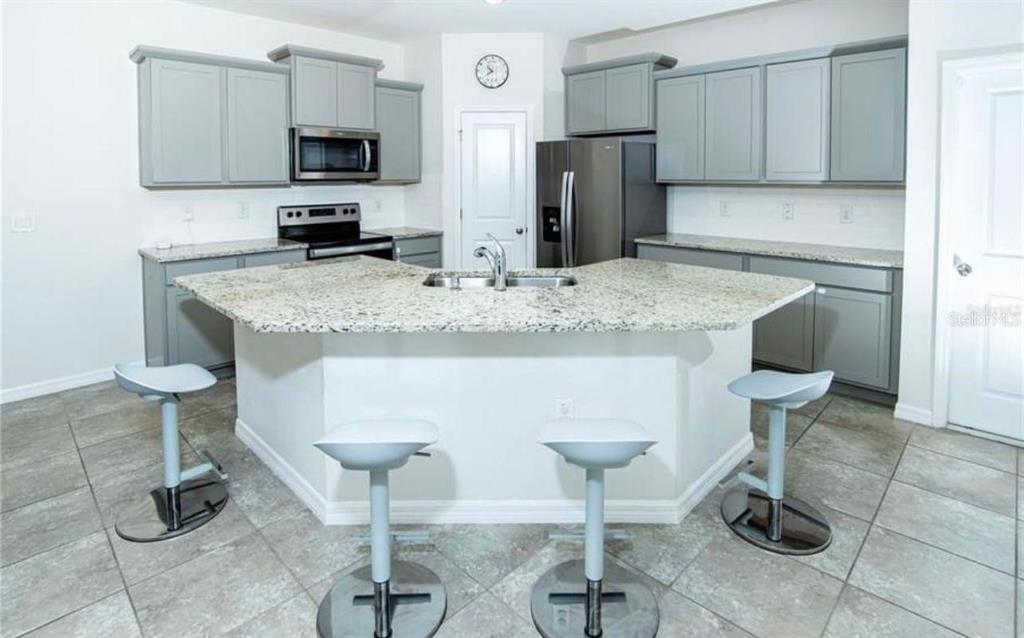 A kitchen features gray cabinets, granite countertops, a central island with stools, and stainless appliances — 7916 STONEBROOK CIRCLE, WESLEY CHAPEL, FL