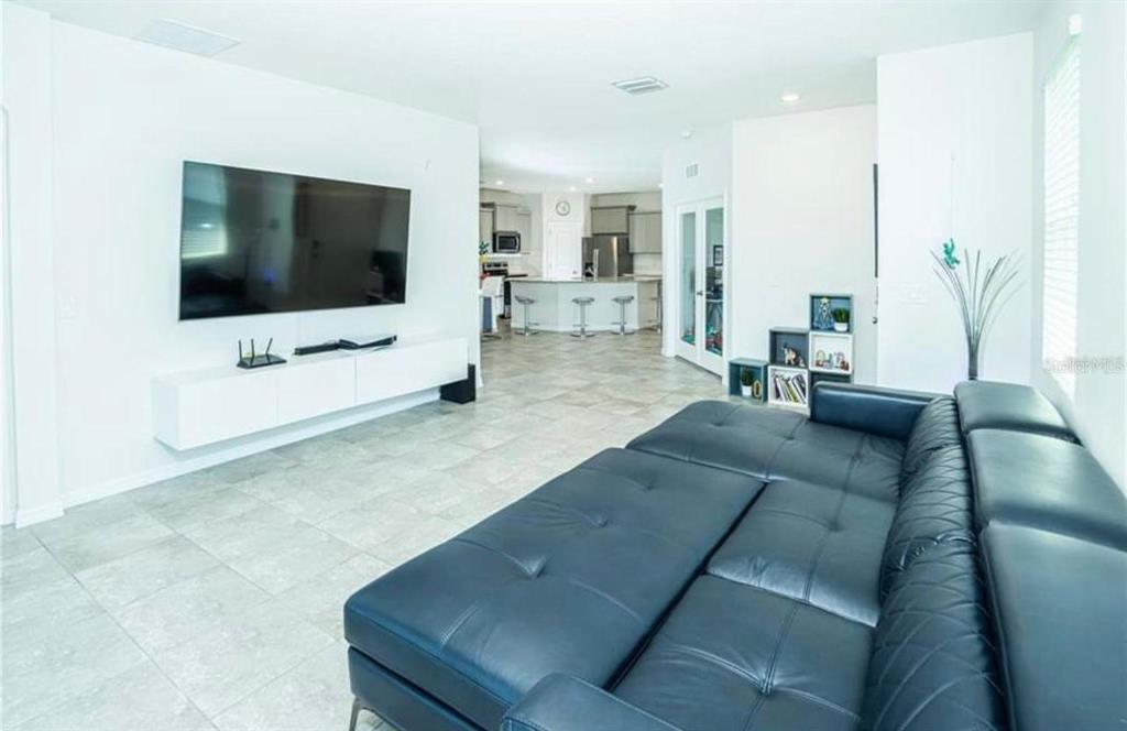 A living room with a large dark leather sofa, wall-mounted television, and tiled flooring — 7916 STONEBROOK CIRCLE, WESLEY CHAPEL, FL