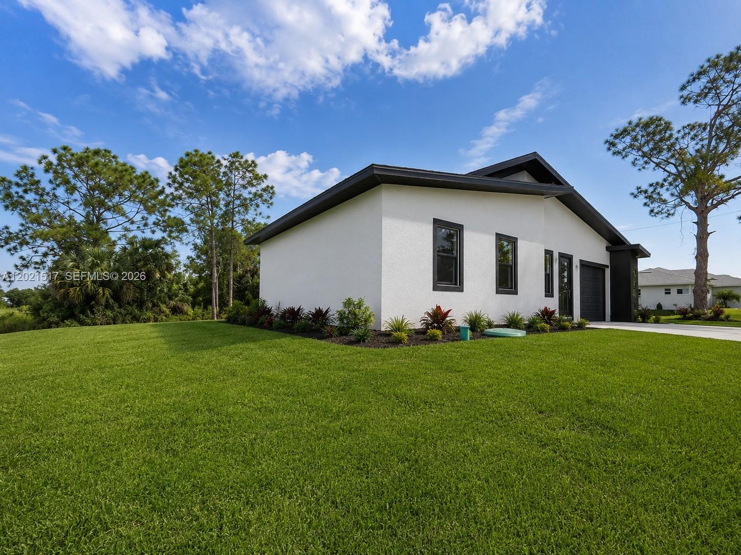 A white single-story house with black trim sits on a grassy lot under a sky — 703 LONG ISLAND, Lehigh Acres FL 33974, LEHIGH ACRES, FL