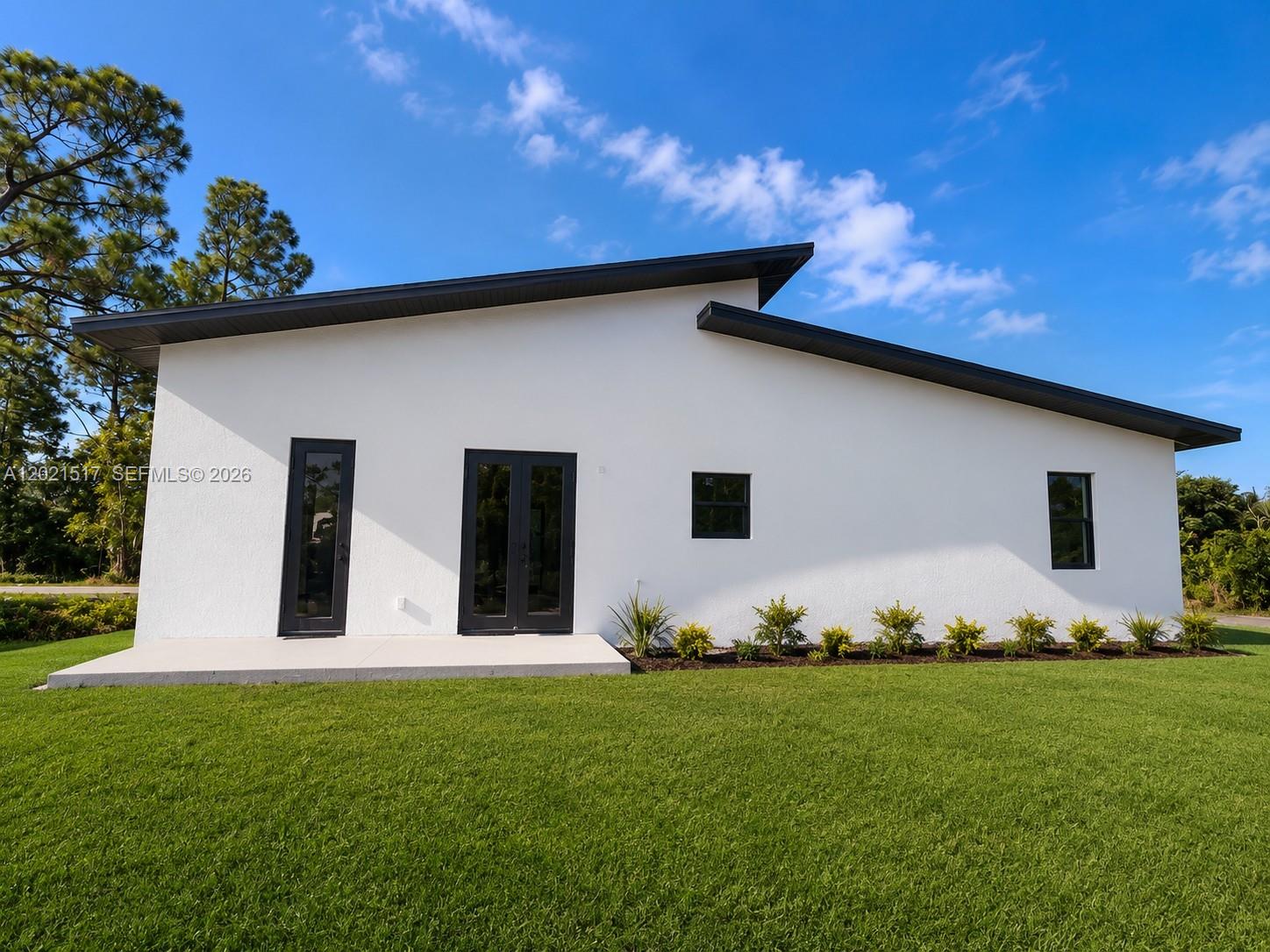 The exterior of a modern white house features black trim, a shed roof, and landscaping — 703 LONG ISLAND, Lehigh Acres FL 33974, LEHIGH ACRES, FL