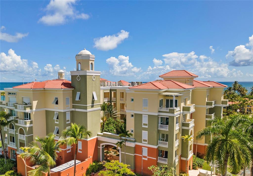 An exterior view of a multi-story Mediterranean-style apartment building with palm trees and ocean views — 100 OCEAN DRIVE UNIT 154, HUMACAO, PR