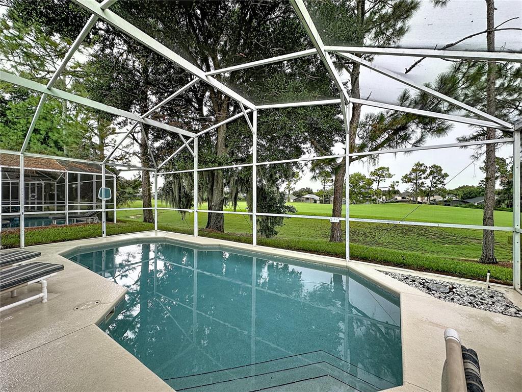 A screened-in swimming pool overlooks a grassy golf course with mature trees — 2464 SAINT AUGUSTINE BOULEVARD, HAINES CITY, FL