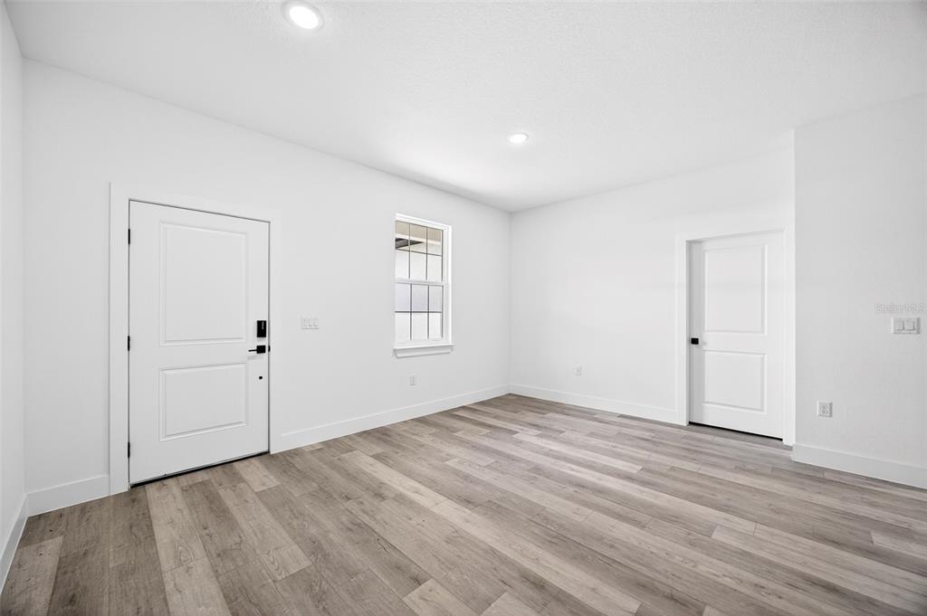 An empty room features white walls, light wood-look flooring, a front door, and a window — 3288 TISHMAN AVENUE, NORTH PORT, FL
