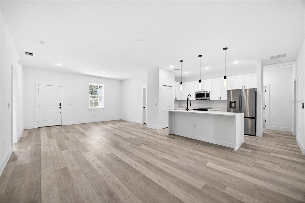 An open-concept kitchen and living area with white cabinetry, stainless steel appliances, and wood-look flooring — 3288 TISHMAN AVENUE, NORTH PORT, FL