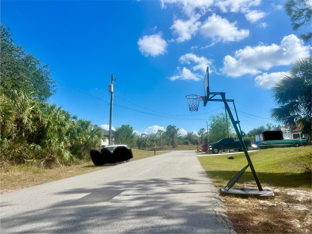 A paved residential street features a basketball hoop on the right and dense foliage nearby — Lot 7 ABBEVILLE ROAD, NORTH PORT, FL